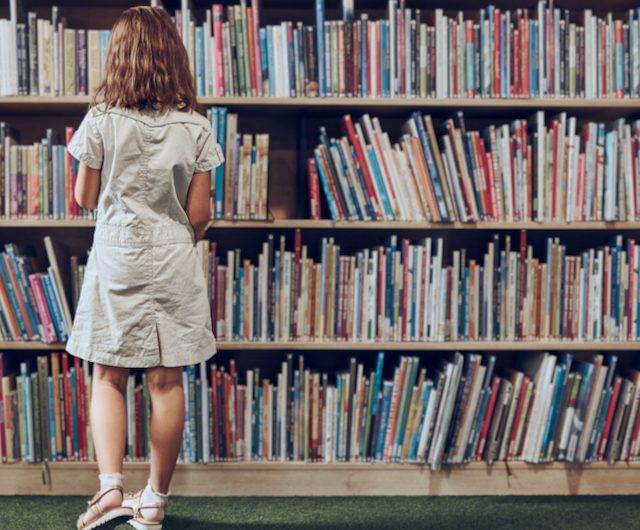 Female student standing in front of a library bookshelf, choosing a book