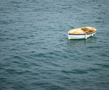 A single wooden rowboat floating on calm water, surrounded by soft, muted tones, symbolizing drift off course.