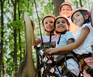 Children navigating a ropes course in a forest.
