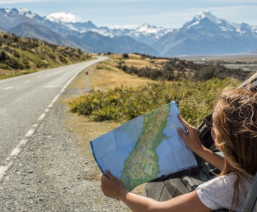 Woman holding a map, leaning out a car window, driving in the mountains