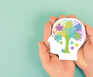 Hands holding a paper head with a colorful tree and puzzle pieces inside.