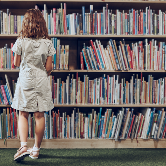 Female student standing in front of a library bookshelf, choosing a book