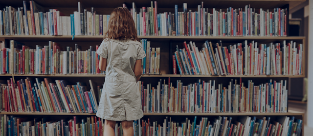 Female student standing in front of a library bookshelf, choosing a book
