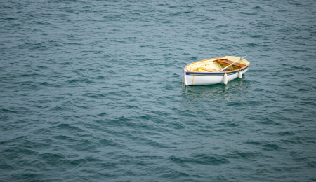 A single wooden rowboat floating on calm water, surrounded by soft, muted tones, symbolizing drift off course.