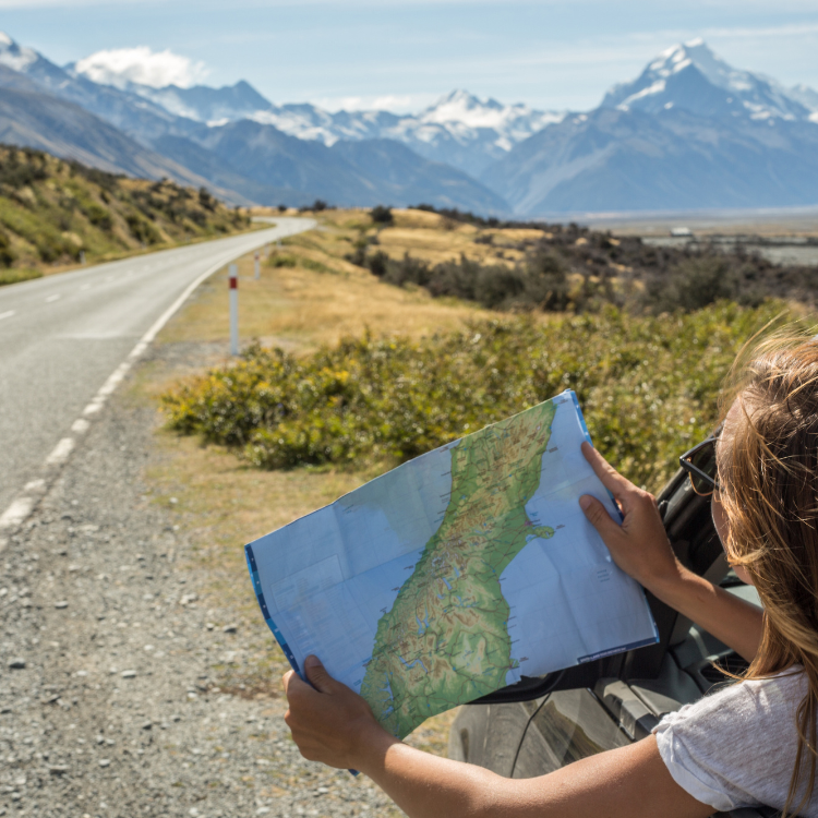 Woman holding a map, leaning out a car window, driving in the mountains