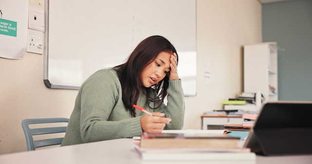 Teacher, a young Asian-American woman, sitting at her desk during a planning session. Visibly frustrated.