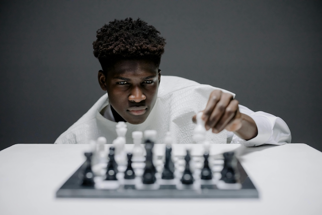 Chess player, a young black man, sits in front of a chess board, poised to make a move